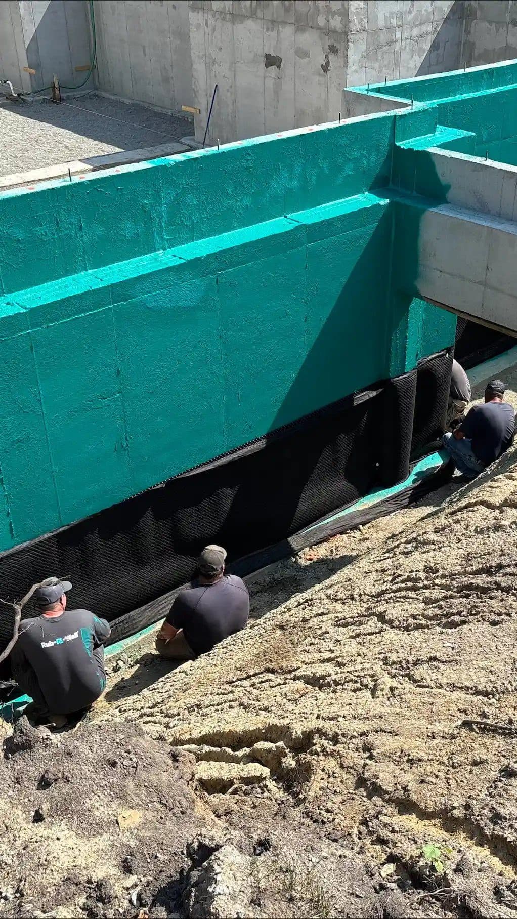 Drainage board installed over teal Rub-R-Wall membrane on a foundation wall